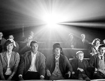 Black and white image of Judi Dench, Jude Hill, Lewis McAskie, Caitriona Balfe, and Jamie Dornan in a movie theater