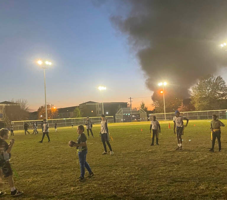 Young people play football at Lanier Park on Tuesday after a junkyard fire sent smoke into the air.