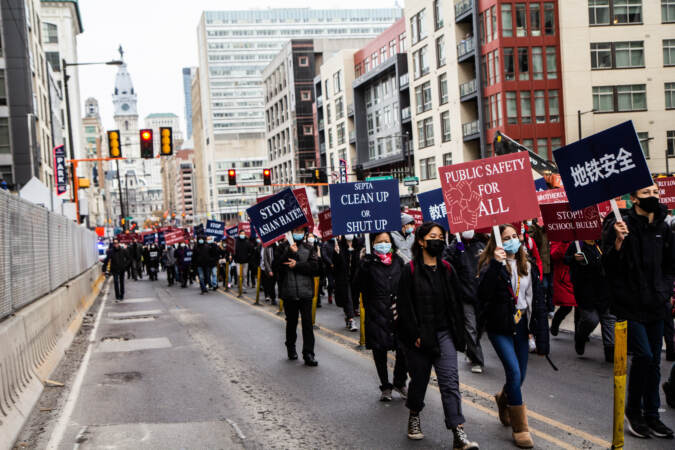 Protesters march down a Philadelphia street with signs that say, 