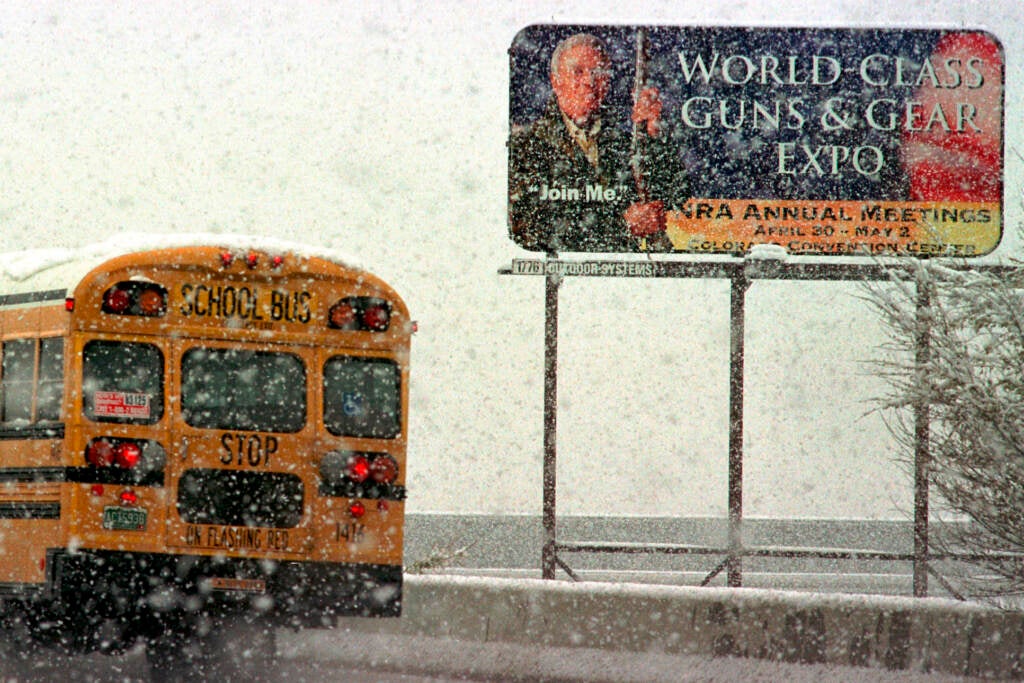 A school bus in 1999 passes a billboard advertising the NRA's annual meeting in Denver