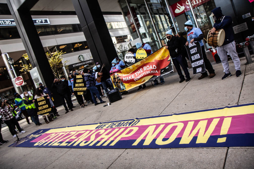 Protesters gather around a sign that says, "Citizenship Now!"