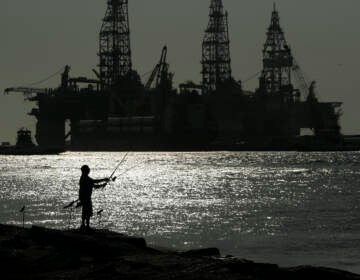 A man wears a face mark as he fishes near docked oil drilling platforms