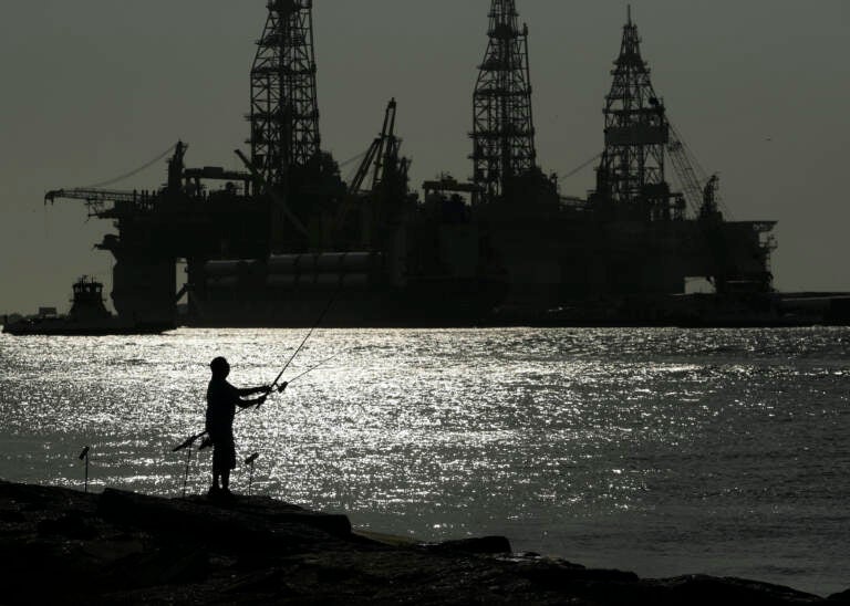 A man wears a face mark as he fishes near docked oil drilling platforms