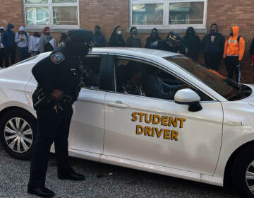 A Wilmington police officer approaches a car with teen drivers during a simulation witnessed by other students at William Penn High School. (Cris Barrish/WHYY)