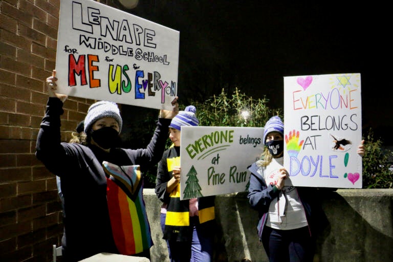 Demonstrators hold sign sin support of LGBTQ people outside a school board meeting