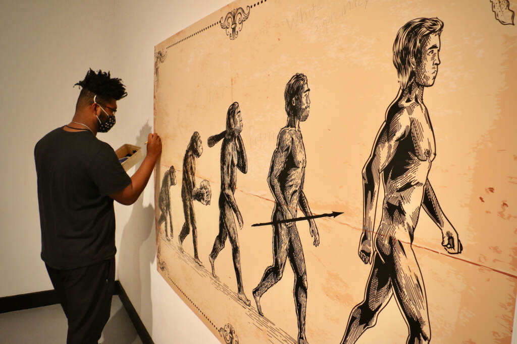 University of Pennsylvania anthropology student Faruq Adger adds words to a print often used in to illustrate the evolution of man. The work is exhibited in the Slought Foundation's exhibit on scientific racism, ''Rotten Foundations, Dangerous Footholds.''