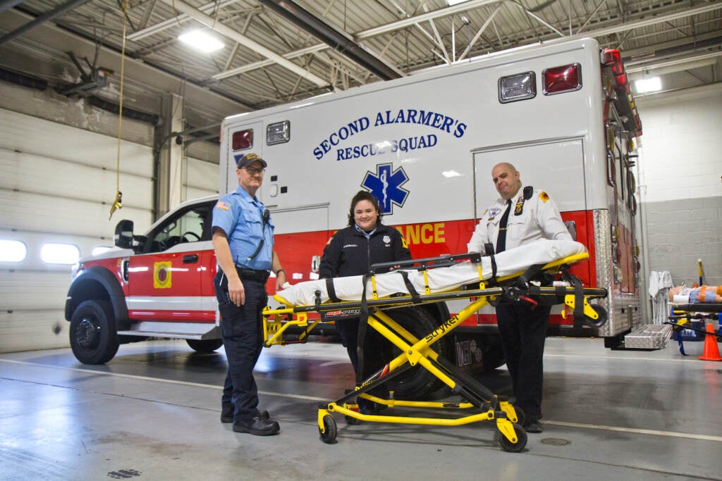 Paramedic John Hill (left), EMT Lizzy O’Driscoll (center), and Assistant Chief Ken Davidson pose in front of an ambulance