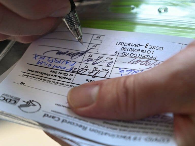 A nurse marks a coronavirus vaccination card with a third 