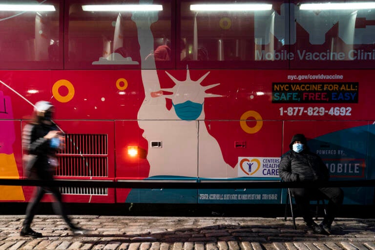 A mobile COVID-19 vaccination and booster shot site operates out of a bus on 59th Street south of Central Park as patients wait on the sidewalk, Thursday, Dec. 2, 2021, in New York. Health officials say multiple cases of the omicron coronavirus variant have been detected in New York, including a man who attended an anime convention in Manhattan in late November and tested positive for the variant when he returned home to Minnesota. (AP Photo/John Minchillo)