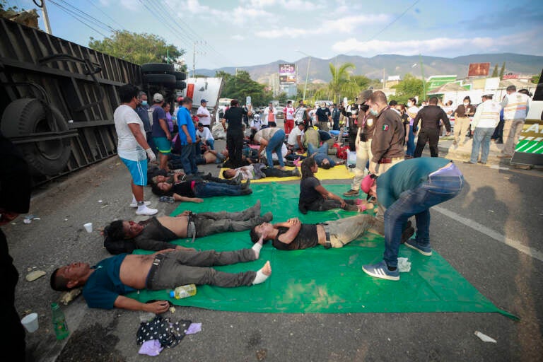 Injured migrants are cared for on the side of the road next to the overturned truck on which they were traveling near Tuxtla Gutierrez, Chiapas state, Mexico, Dec. 9, 2021. Mexican authorities say at least 49 people were killed and dozens more injured when the truck carrying the migrants rolled over on the highway in southern Mexico