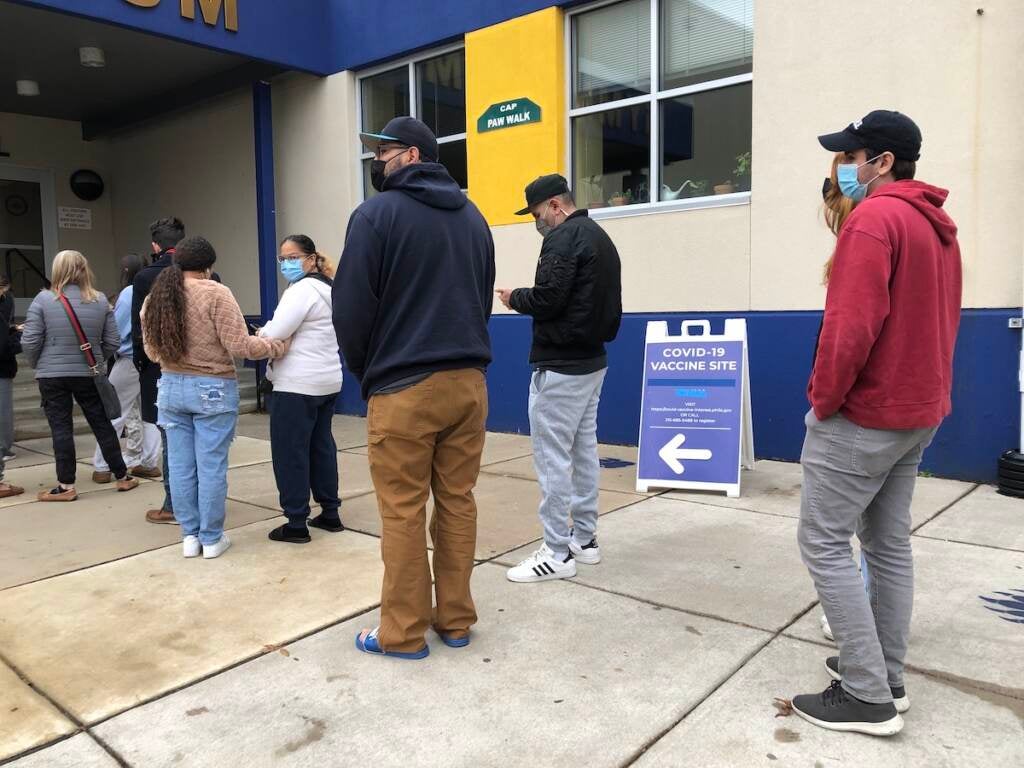 People wait in line to get doses of COVID vaccines and free rapid, at-home test kits at a city-run event in the Harrowgate neighborhood