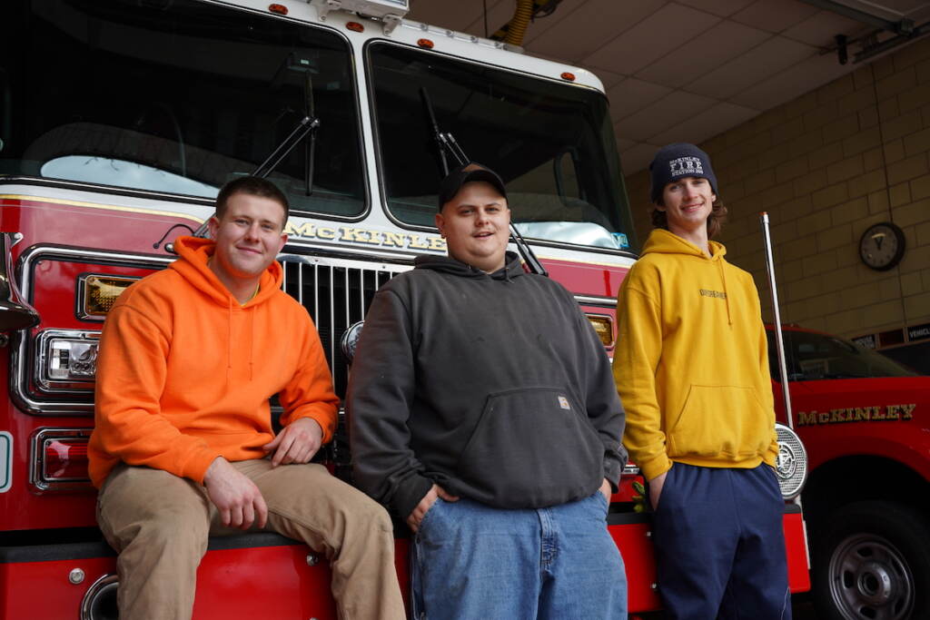 McKinley’s volunteer firefighters (from left) Evan Metz, Zach Liss, and Brendan Tracey hold down the fort and sell trees during the Christmas event. (Kenny Cooper/WHYY)