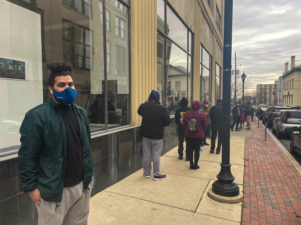 Anthony Beltran poses for a photo while waiting in line, wearing a mask