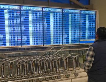 A man looks at the departures board at Salt Lake City International Airport Friday, Dec. 24, 2021, in Salt Lake City. At least three major airlines say they have canceled dozens of flights because illnesses largely tied to the omicron variant of COVID-19 have taken a toll on flight crew numbers during the busy holiday travel season.