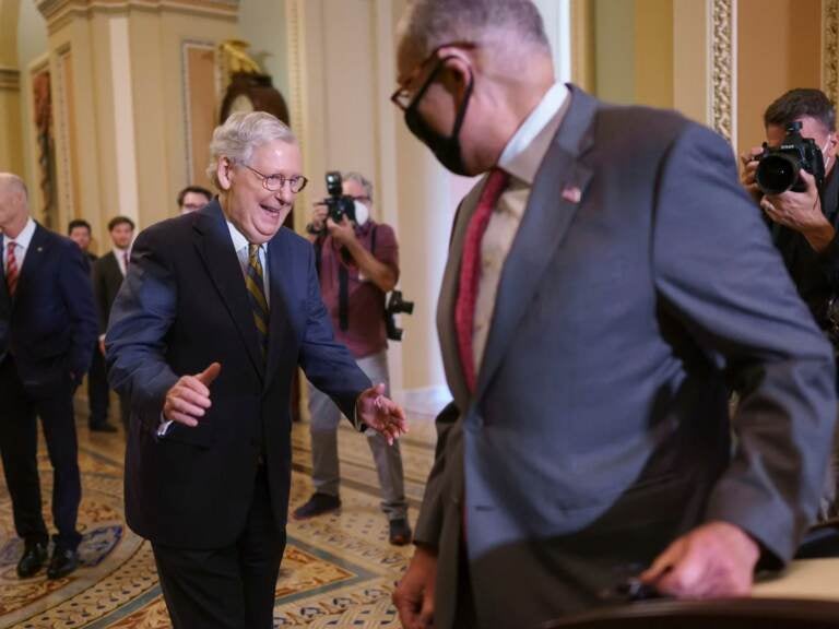 In this Aug. 3, 2021, photo, Senate Democratic Leader Chuck Schumer, of New York, and Senate Republican Leader Mitch McConnell, of Kentucky, left rear, smile when they both arrived at the same time to speak to reporters about progress on infrastructure bill, at the Capitol in Washington. Senators are convening for a rare weekend session on the bipartisan infrastructure bill as they edge toward a vote. Saturday's action in the Senate could wrap up swiftly with passage of the $1 trillion package or drag out for days by opponents trying to slow President Joe Biden’s big priority.