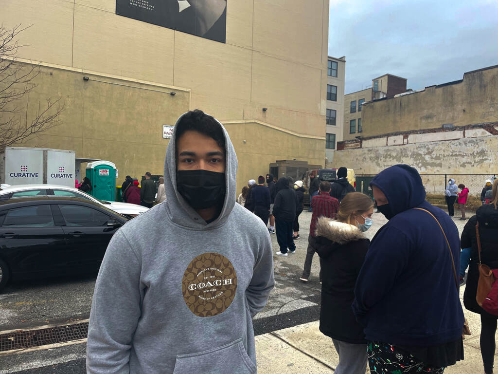 Carlos Mendez poses for a photo while waiting in line, wearing a mask