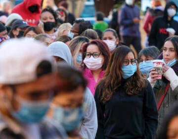 Shoppers wearing face masks wait in line to enter a store