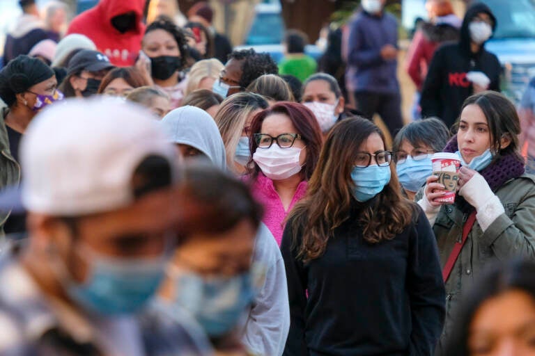 Shoppers wearing face masks wait in line to enter a store