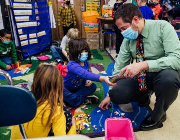 Principal Palazzo kneels beside students building with Legos so they can show him their progress during recess in a first grade classroom.