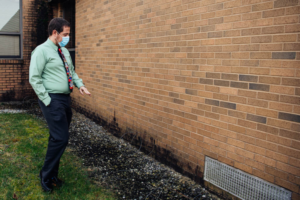 On the outside of the building, Principal Palazzo gestures at the wall to show water levels when the courtyard floods