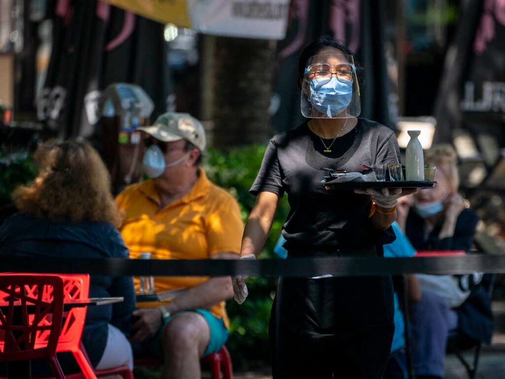 A waiter at Raku wears a face mask while serving customers outdoors