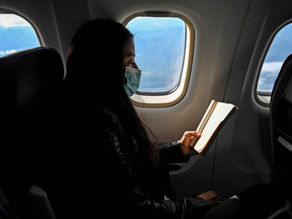 A passenger wearing a face mask reads a book on an airplane