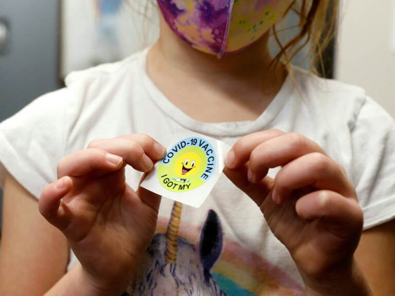 A 6-year-old child holds a sticker she received after getting the Pfizer-BioNTech COVID-19 vaccine