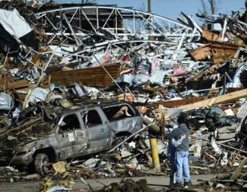 Two people share an embrace while surrounded by the damage left from a tornado