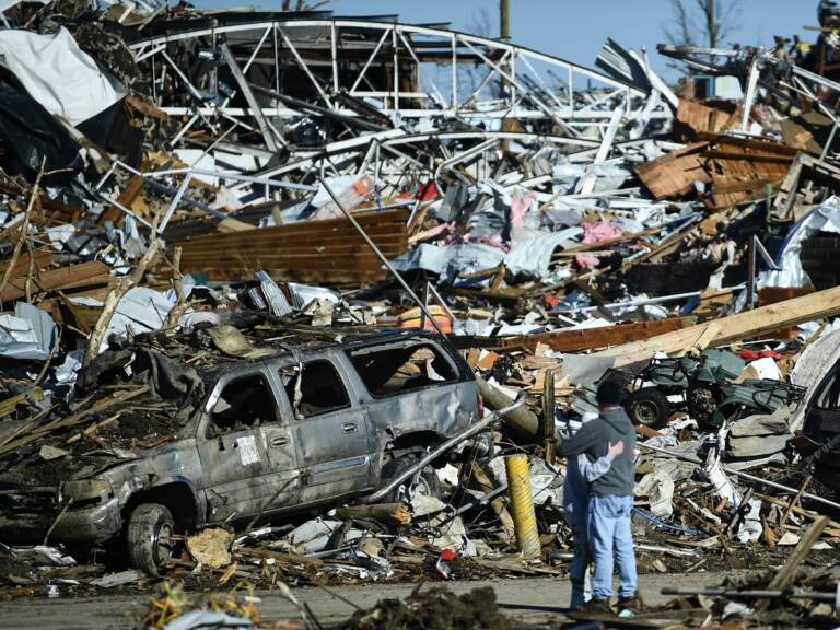 Two people share an embrace while surrounded by the damage left from a tornado