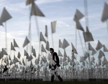 A person wearing a face covering walks past a white flag memorial installation outside Griffith Observatory honoring the nearly 27,000 Los Angeles County residents who have died from COVID-19 on November 18, 2021 in Los Angeles, California. (Photo by Mario Tama/Getty Images)