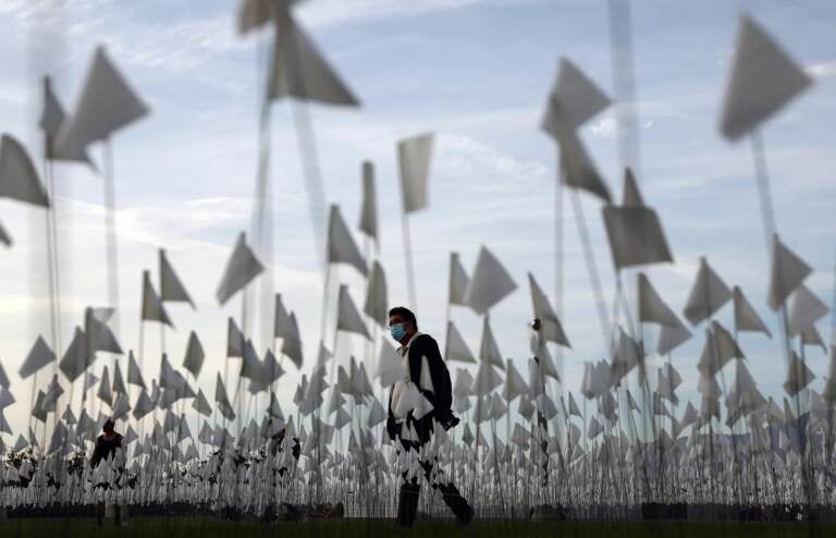 A person wearing a face covering walks past a white flag memorial installation outside Griffith Observatory honoring the nearly 27,000 Los Angeles County residents who have died from COVID-19 on November 18, 2021 in Los Angeles, California. (Photo by Mario Tama/Getty Images)