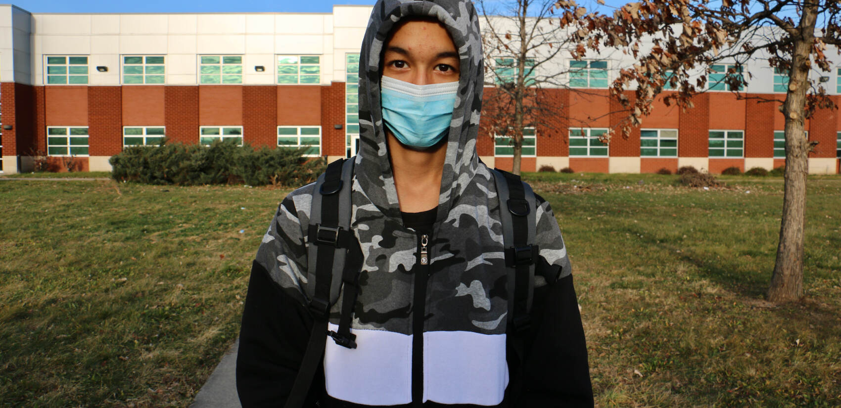 Ali Wahaj Mosakhil wears a mask while standing in front of a school