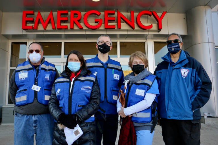 Volunteers from the Delaware County Medical Reserve Corps stand outside the Crozer Emergency Room, where they are needed to help the hospital cope with a flood of COVID-19 patients. They are (from left) Ken Barton, Marlynn Orlando, Georg Strey, Nancy Niemiec, and Dennis Daye.(Emma Lee/WHYY)