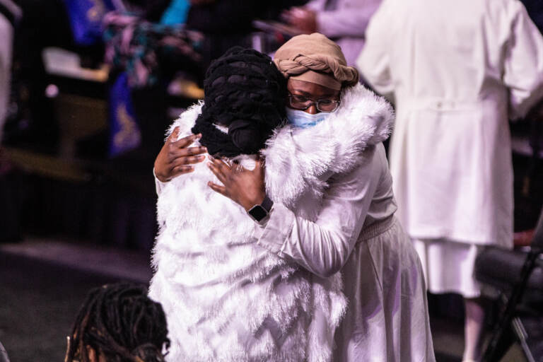 Two people comfort one another at a funeral service
