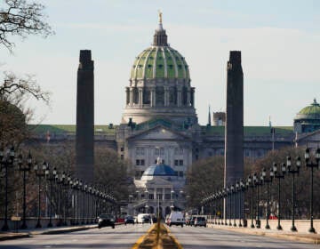 The Pennsylvania Capitol building in Harrisburg is shown from afar, with the road stretching towards it.