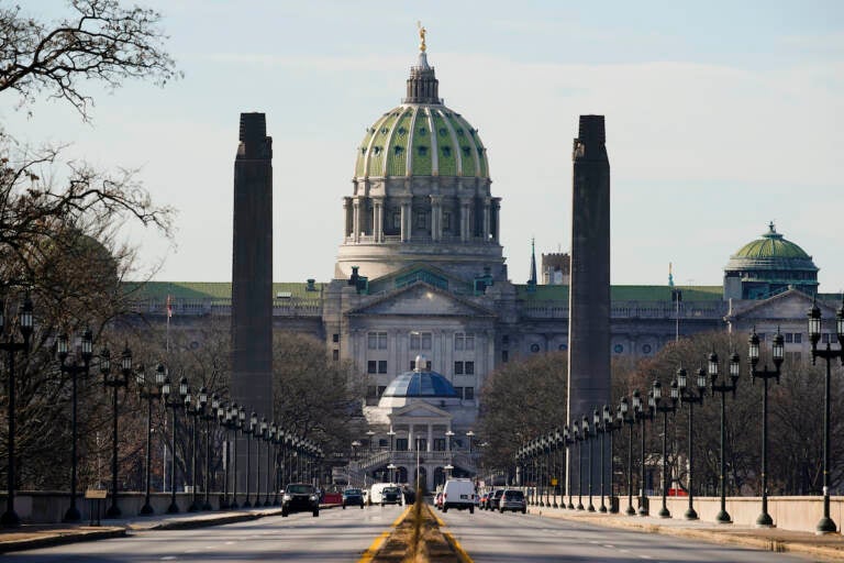 The Pennsylvania Capitol building in Harrisburg is shown from afar, with the road stretching towards it.