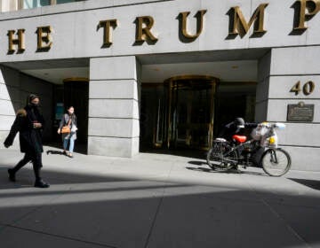 FILE - Pedestrians and a food delivery man are seen outside the Trump building at 40 Wall Street in New York's Financial District, Tuesday, March 23, 2021.  The New York attorney general, Tuesday, Jan. 18, 2022, says her investigators have uncovered evidence that former President Donald Trump's company used 'fraudulent or misleading' valuations of its golf clubs, skyscrapers and other property to get loans and tax benefits. (AP Photo/Mary Altaffer)