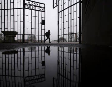 A person walks behind the gate of the Sachsenhausen Nazi death camp with the phrase 'Arbeit macht frei' (work sets you free) in Oranienburg, about 30 kilometers (18 miles) north of Berlin, Germany, Tuesday, Jan. 25, 2022. On Thursday Jan. 27, 2022 the International Holocaust Remembrance Day marks the liberation of the Auschwitz Nazi death camp on Jan. 27, 1945. (AP Photo/Markus Schreiber)