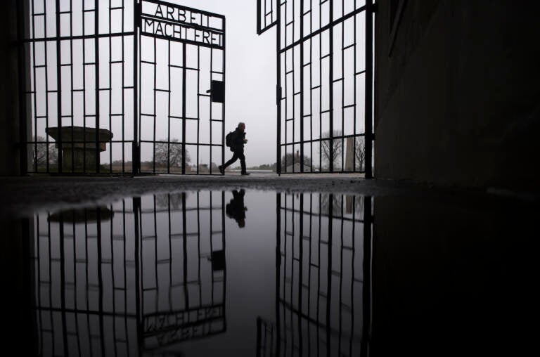 A person walks behind the gate of the Sachsenhausen Nazi death camp with the phrase 'Arbeit macht frei' (work sets you free) in Oranienburg, about 30 kilometers (18 miles) north of Berlin, Germany, Tuesday, Jan. 25, 2022. On Thursday Jan. 27, 2022 the International Holocaust Remembrance Day marks the liberation of the Auschwitz Nazi death camp on Jan. 27, 1945. (AP Photo/Markus Schreiber)