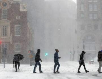 People cross Congress Street, Saturday, Jan. 29, 2022, in Boston. Forecasters watched closely for new snowfall records, especially in Boston, where the heaviest snow was expected late Saturday. (AP Photo/Michael Dwyer)