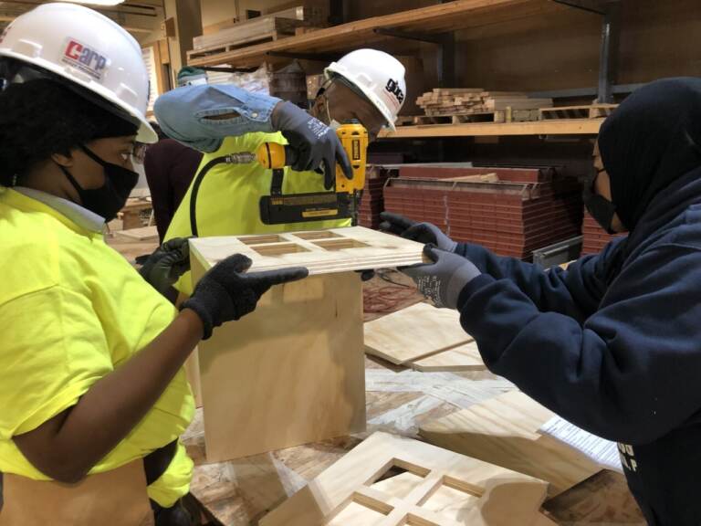 An experienced carpenter helps two CARP apprentices build a little free library.(Emily Rizzo/WHYY)