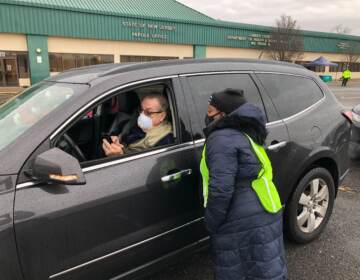 Koren Norwood, a Camden County health educator, assists Steve Shirk, of Audobon, with the COVID test packet, which includes a QR code to get to the website. Shirk was one of dozens to arrive to a new drive-in COVID testing site in Camden on Jan. 5, 2022. (P. Kenneth Burns/WHYY)