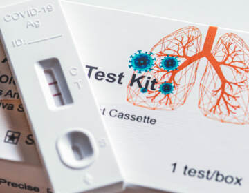 A close up of a positive Covid-19 antigen test kit and box with an illustration of lungs and a virus particle