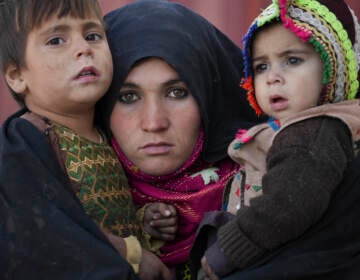 An Afghan woman holds her children as she waits for a consultation outside a makeshift clinic organized by World Vision in an IDP settlement near Herat, Afghanistan, Thursday, Dec. 16, 2021. (AP Photo/Mstyslav Chernov)