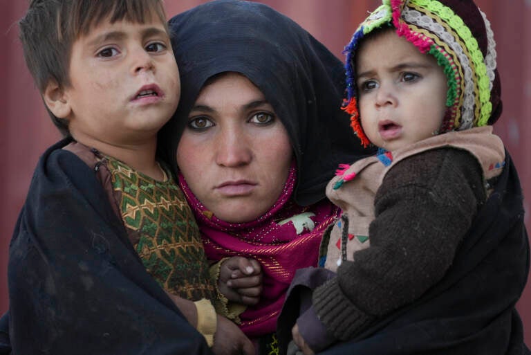 An Afghan woman holds her children as she waits for a consultation outside a makeshift clinic organized by World Vision in an IDP settlement near Herat, Afghanistan, Thursday, Dec. 16, 2021. (AP Photo/Mstyslav Chernov)