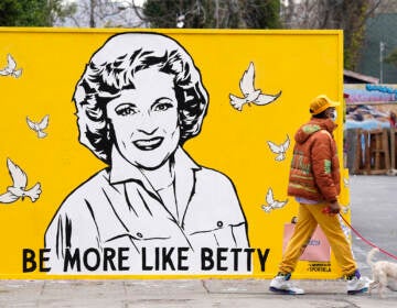 A man walks a dog past a new mural of the late actress Betty Whit