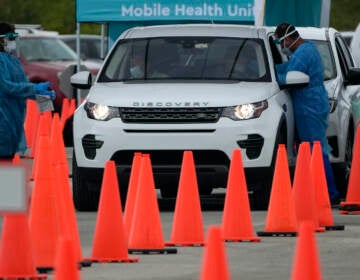 Health care workers administer nasal swabs to drivers and passengers at a drive-thru COVID-19 testing site