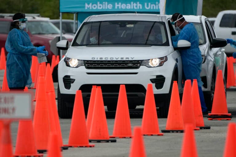 Health care workers administer nasal swabs to drivers and passengers at a drive-thru COVID-19 testing site