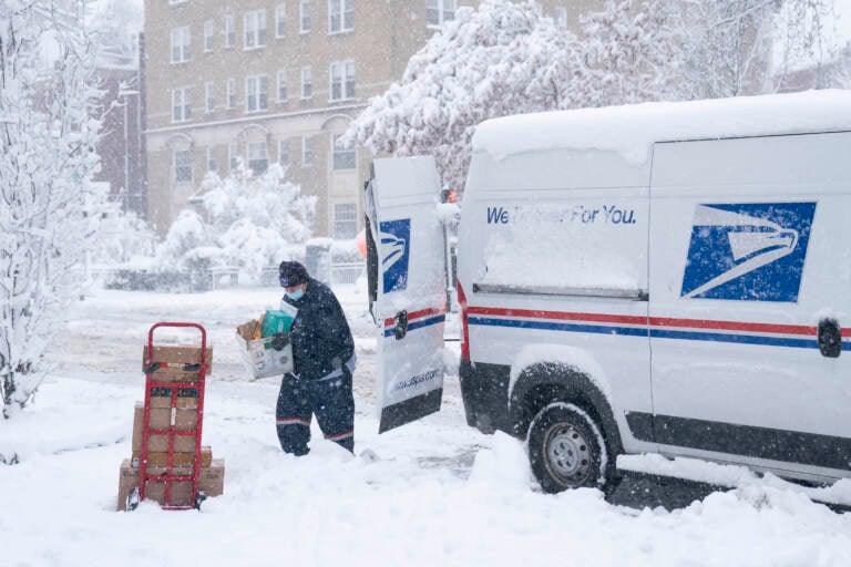 A postal worker carries packages through the snow