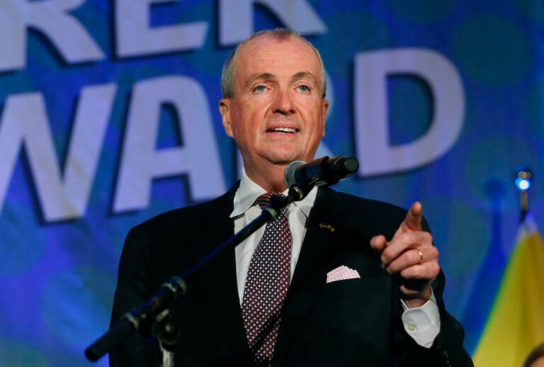 New Jersey Gov. Phil Murphy gestures while standing behind a mic